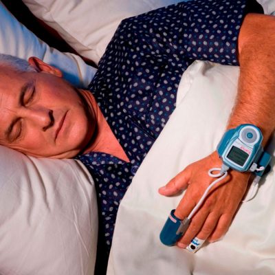 Man sleeping in bed with device attached to finger and wrist